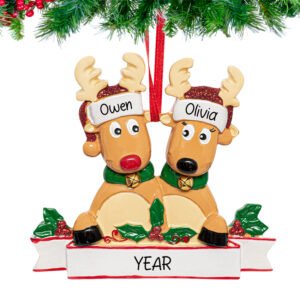 Two reindeer figurines nestled t, personalized with custom names and year, hanging from a snow-dusted pine branch.